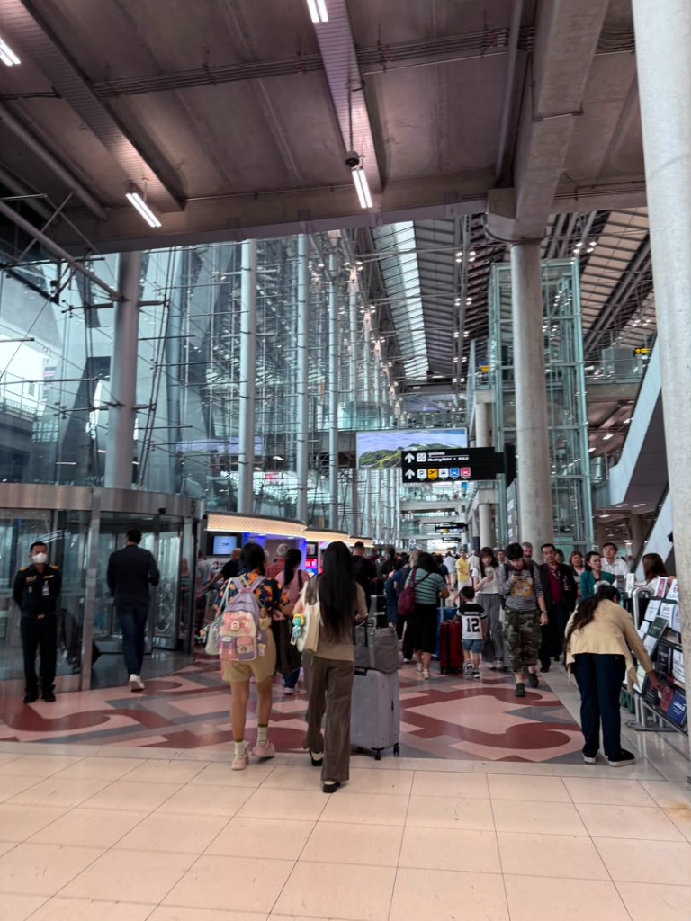 Crowded arrivals hall at Suvarnabhumi Airport with overhead signs for taxi, van, and Airport Rail Link